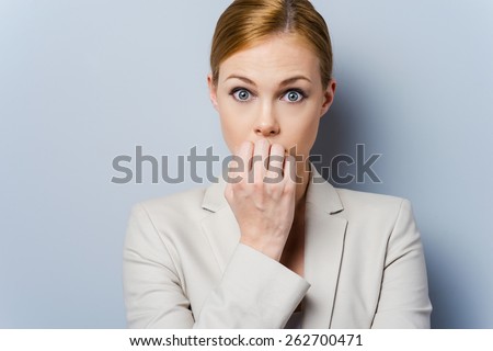 A little bit nervous. Nervous young businesswoman biting her nails while standing against grey background