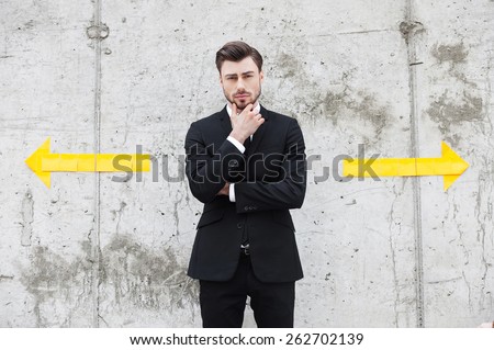 Facing the choice. Thoughtful young man in formalwear holding hand on chin while standing outdoors