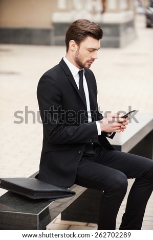 Staying connected anytime and anywhere. Confident young man in formalwear holding mobile phone while sitting outdoors