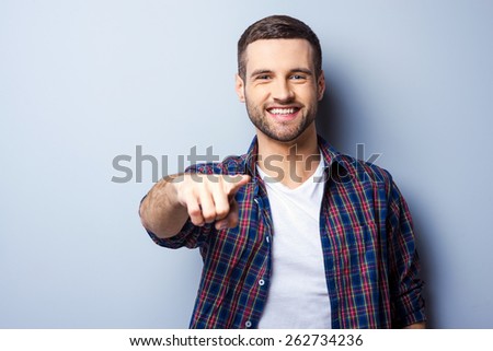 I choose you! Portrait of handsome young man in casual shirt pointing you and smiling while standing against grey background