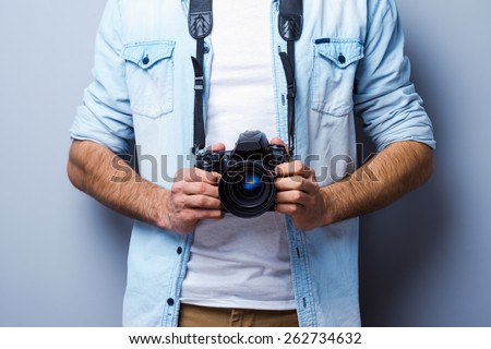 Man with digital camera. Cropped image of man with digital camera standing against grey background