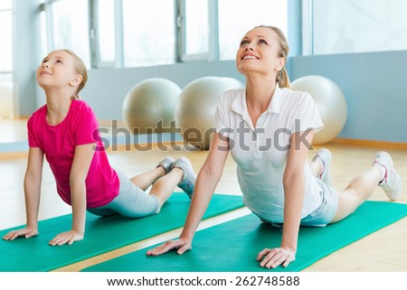 Warming up in sports club. Cheerful mother and daughter doing stretching exercises while lying on exercise mats in sports club