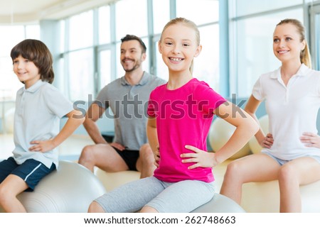 I love my sporty family! Happy little girl looking at camera and smiling while exercising with her family in sports club
