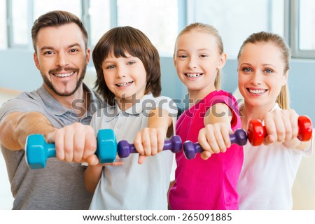 Living a healthy life together. Happy family holding different sports equipment while standing close to each other in health club