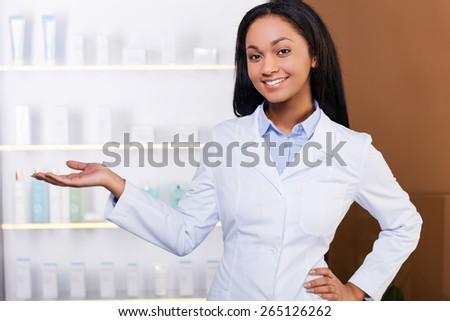Make your choice. Beautiful young African woman in lab coat keeping arms crossed and smiling while standing in drugstore