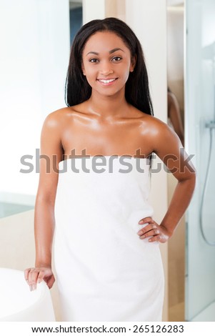 Fresh and beautiful. Beautiful young African woman wrapped in a towel looking at camera and smiling while standing in bathroom