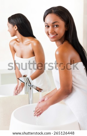 Keeping her body clean and fresh. Beautiful young African woman washing hands in bathroom and looking over shoulder