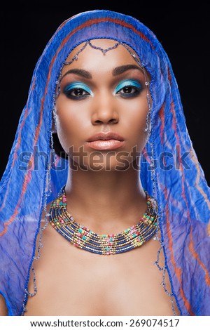 Fascinating beauty. Beautiful African woman covering head by scarf and looking at camera while standing against black background