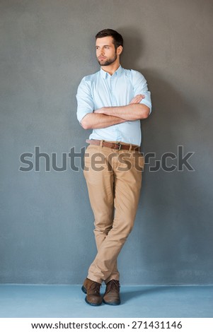 Serious and confident. Full length of handsome young man in shirt keeping arms crossed and looking away while standing against grey background