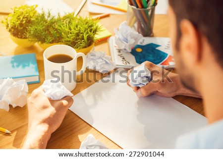 It is always hard to start. Close-up rear view of man smashing pieces of paper while sitting at his working place