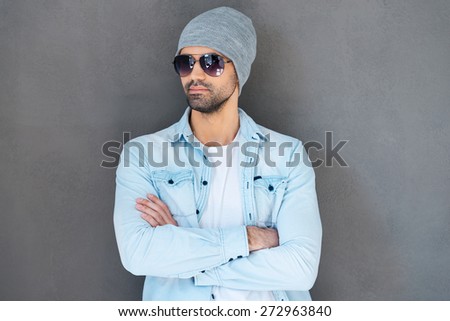 Looking so cool. Handsome young man in eyewear keeping arms crossed while standing against grey background