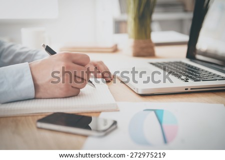 Making some urgent notes. Close-up of man writing something in his note pad while sitting at his working place