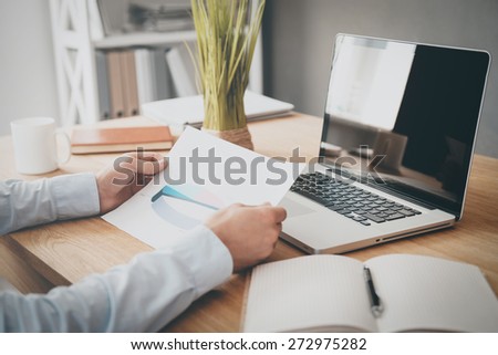 Businessman examining diagram. Close-up of man holding paper with diagram on it while sitting his working place