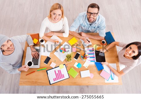 Successful creative team. Top view of group of business people in smart casual wear working together and smiling while sitting at the wooden desk