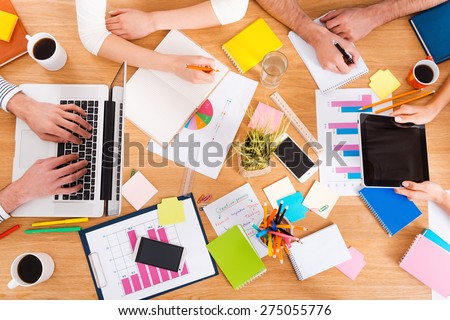 Creative working process. Top view close-up image of people working together while sitting at the wooden desk