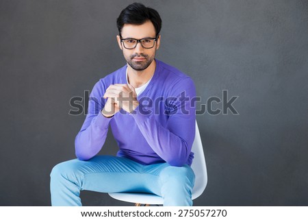 Keeping calm in his chair. Full length of handsome young man looking at camera while sitting against grey background