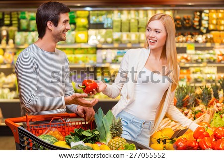 Shopping is a fun. Happy young women giving red pepper to her boyfriend while shopping in a food store