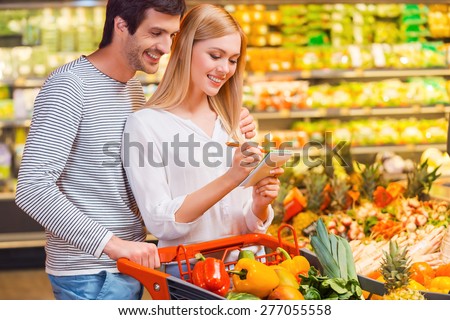 Choosing only healthy food. Happy young couple bonding to each other and smiling while shopping in a food store
