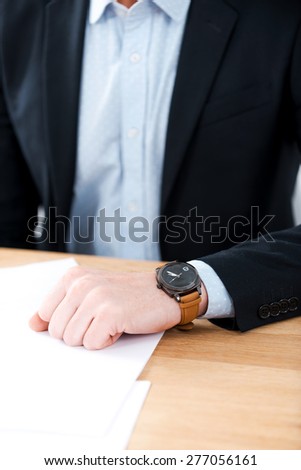 Time for business. Close-up of businessman wearing watch on his hand while sitting at his working place