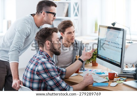 Collaboration is a key to success. Three young business people discussing something while looking at the computer monitor together