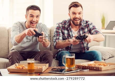 The avid gamers. Two young happy men playing video games while sitting on sofa