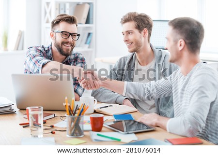 Sealing a deal. Business people shaking hands while sitting at the desk in office