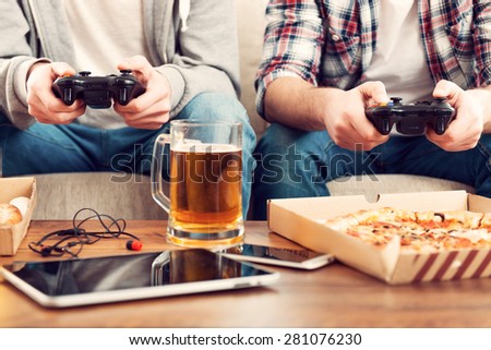 Playing video games. Close-up of two men playing video games while sitting on sofa