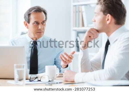 Wise advice for business nice. Two business people in formalwear discussing something while sitting at working place