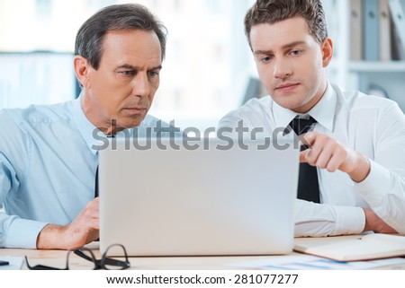 Searching for smart solutions together. Two serious business people in formalwear discussing something and looking at laptop while sitting at working place