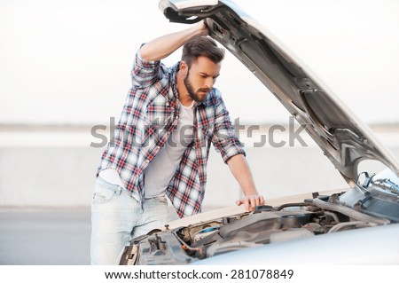 Car breakdown. Concentrated young man holding hands on vehicle hood and looking inside it while standing outdoors