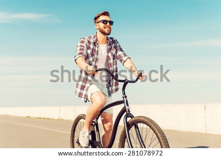Best way to start a day. Happy young man in eyewear riding bicycle and smiling