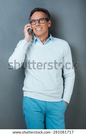 Good talk. Happy mature man talking on the mobile phone and smiling while standing against grey background