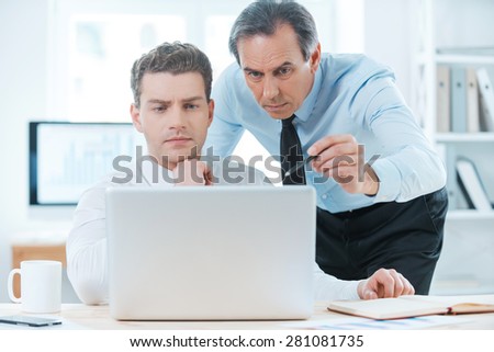 Sharing experience with colleague. Two serious business people in formalwear discussing something and looking at laptop