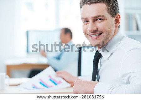 Handsome businessman at work.Happy businessman in formalwear looking over shoulders and smiling at camera while sitting at his desk in office