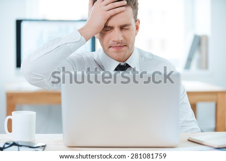 Oh no! Frustrated businessman working on laptop and touching his head while sitting at his working place