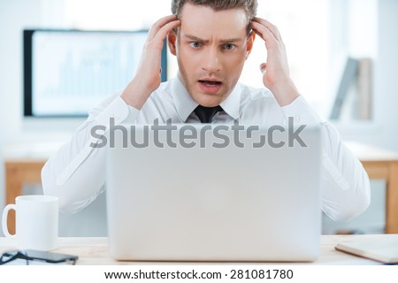 Business troubles. Frustrated businessman working on laptop and touching his head while sitting at his working place
