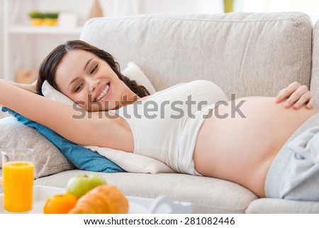Healthy eating for me and my baby. Happy pregnant woman looking on her meal and smiling while lying on a couch