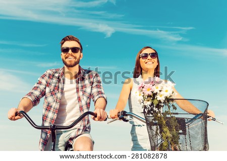 Keep calm and ride on. Low angle view of cheerful young couple smiling and riding on bicycles