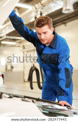 Examining car. Concentrated young man in uniform examining car while standing in workshop