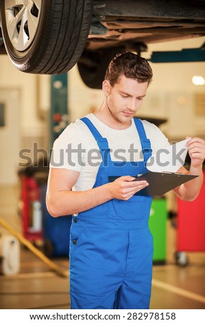 Checking every detail. Confident young man in uniform holding clipboard while standing in workshop