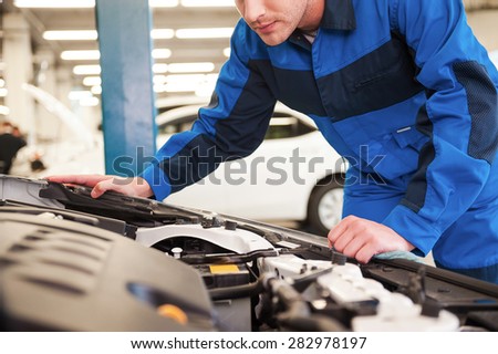 Trust your car to the experts. Close-up of concentrated young man in uniform examining car while standing in workshop