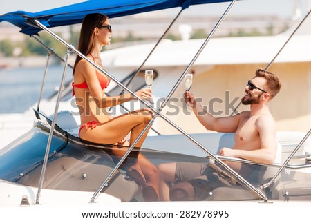 When nothing else matters. Cheerful young couple holding glasses with champagne while sitting on the board of yacht
