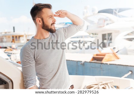 Opening new horizons. Confident young man looking forward and smiling while standing on the board of yacht