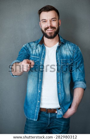He knows what he wants!Cheerful young man pointing you and smiling at camera while standing against grey background