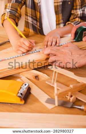 Skilled little carpenter.Seriousboy making measurements on the wooden plank while his father helping him