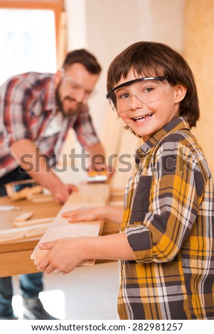 Little carpenter. Cheerful little boylooking at camera over shoulder while working with his father in workshop