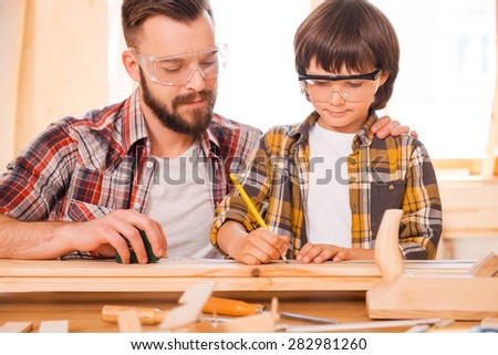 One day you will be a talented carpenter. Concentrated young male carpenter teaching his son to work with wood in his workshop