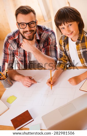 Turning their dreams to reality. Concentrated young man using compass for drawing while sitting at his workplace with his son
