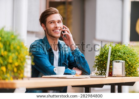 Fresh air for fresh ideas. Cheerful young man talking on the mobile phone and smiling while sitting at sidewalk cafe
