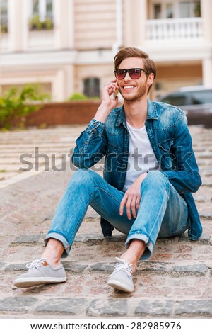 In touch with his friends. Confident young man talking on the mobile phone while sitting outdoors